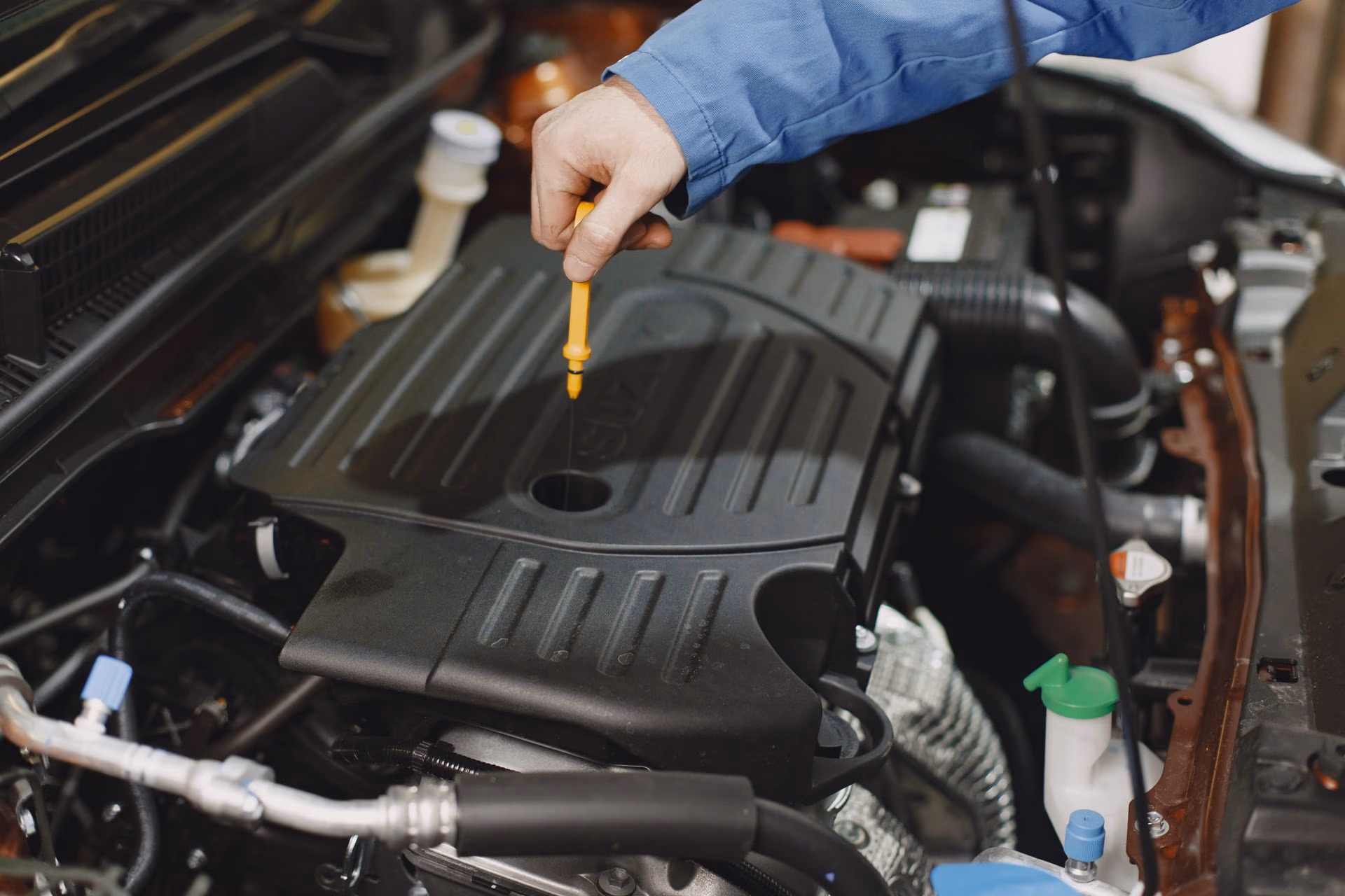 Person checking the engine oil level using a dipstick in a car engine compartment.