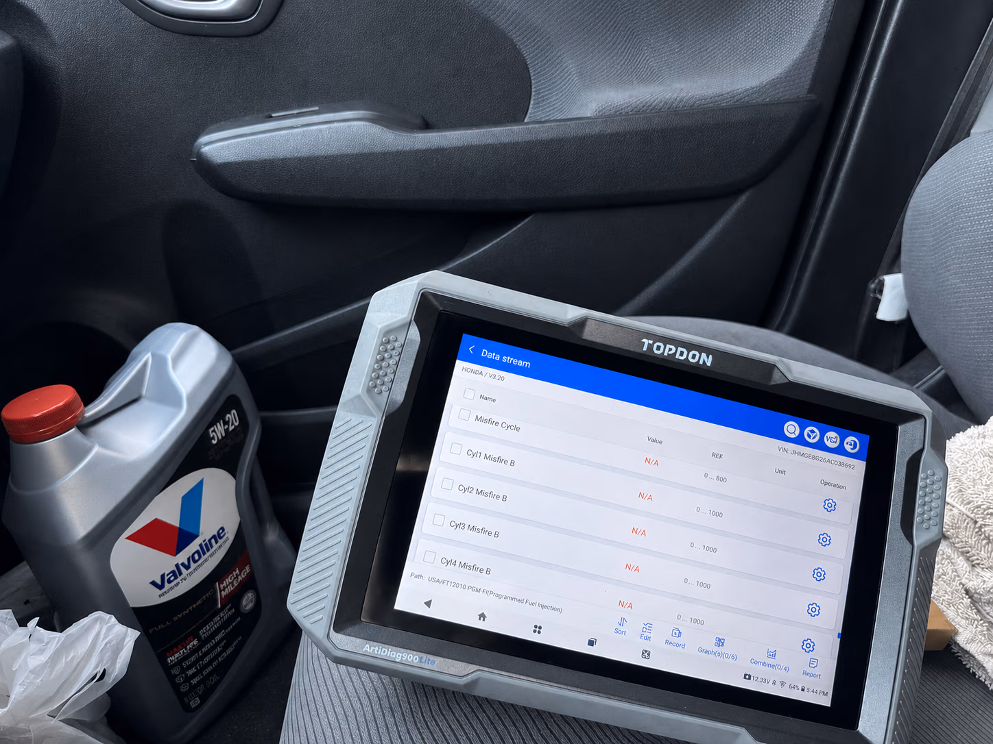 TOPDON diagnostic tablet showing misfire data for a Honda, next to a Valvoline 5W-20 oil container.