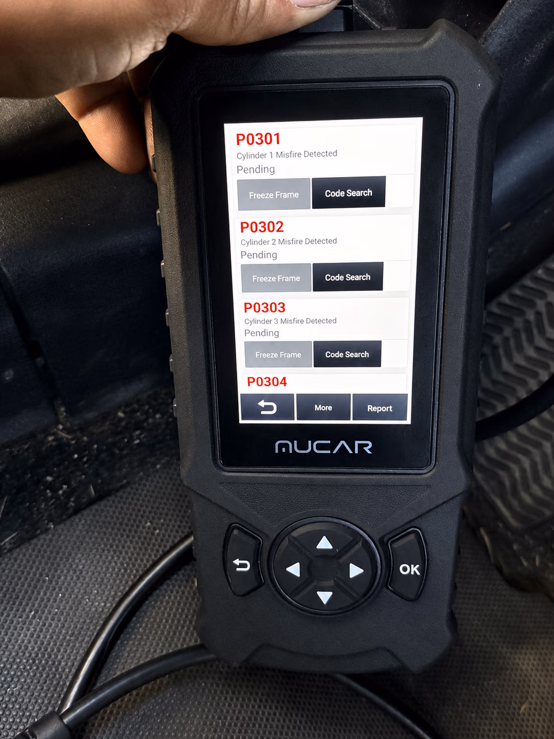 Hand holding MUCAR scanner displaying cylinder misfire codes P0301, P0302, and P0303 pending.
