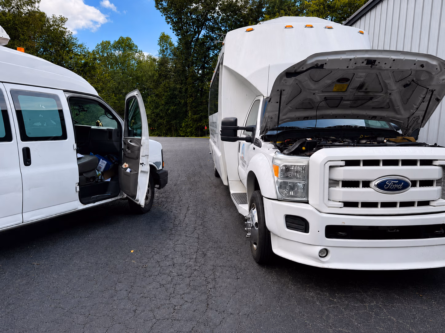 White Ford van with hood open parked beside a white van with the driver's door open outdoors.