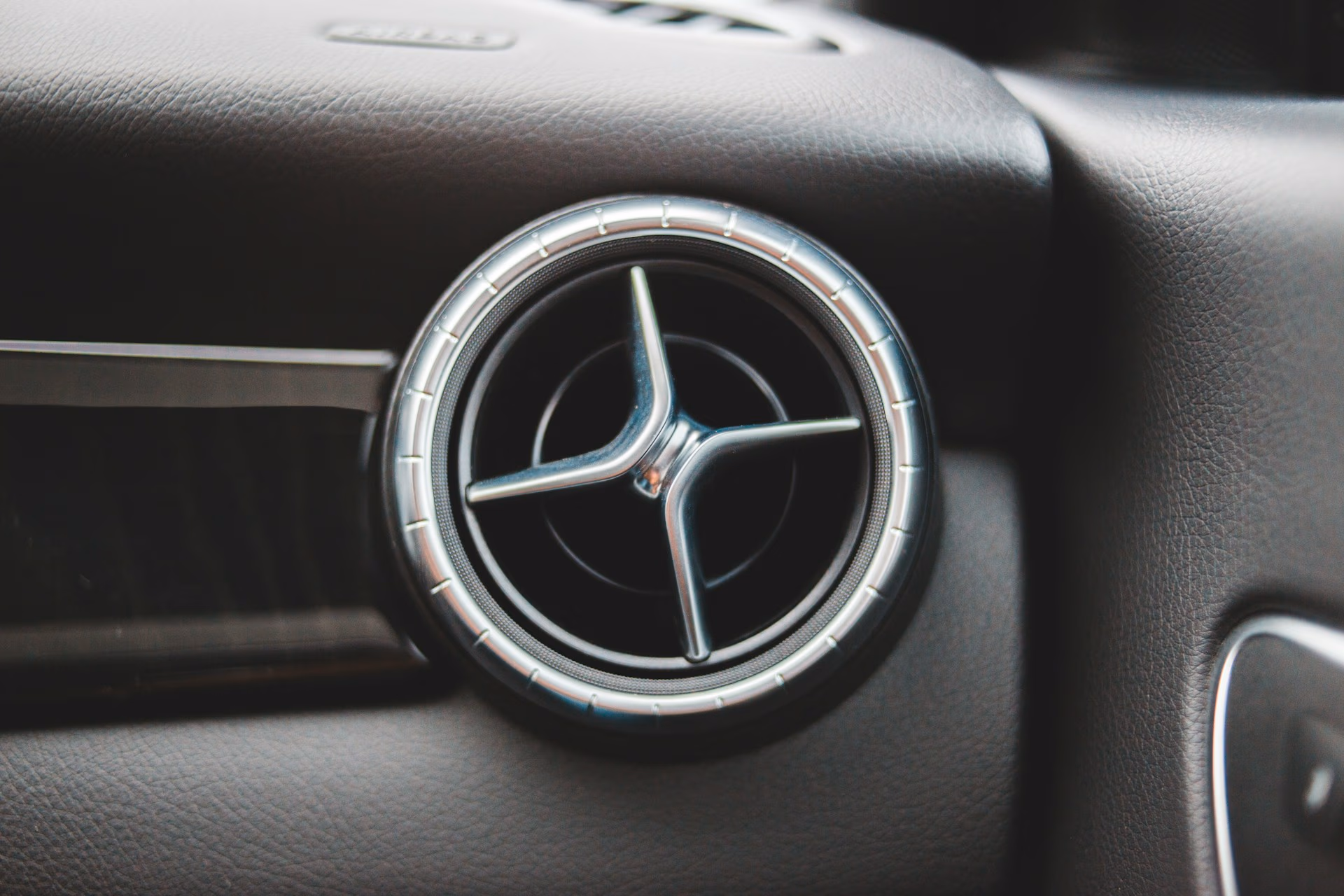 Close-up of a round car air vent with a silver trim and three metal fins inside.