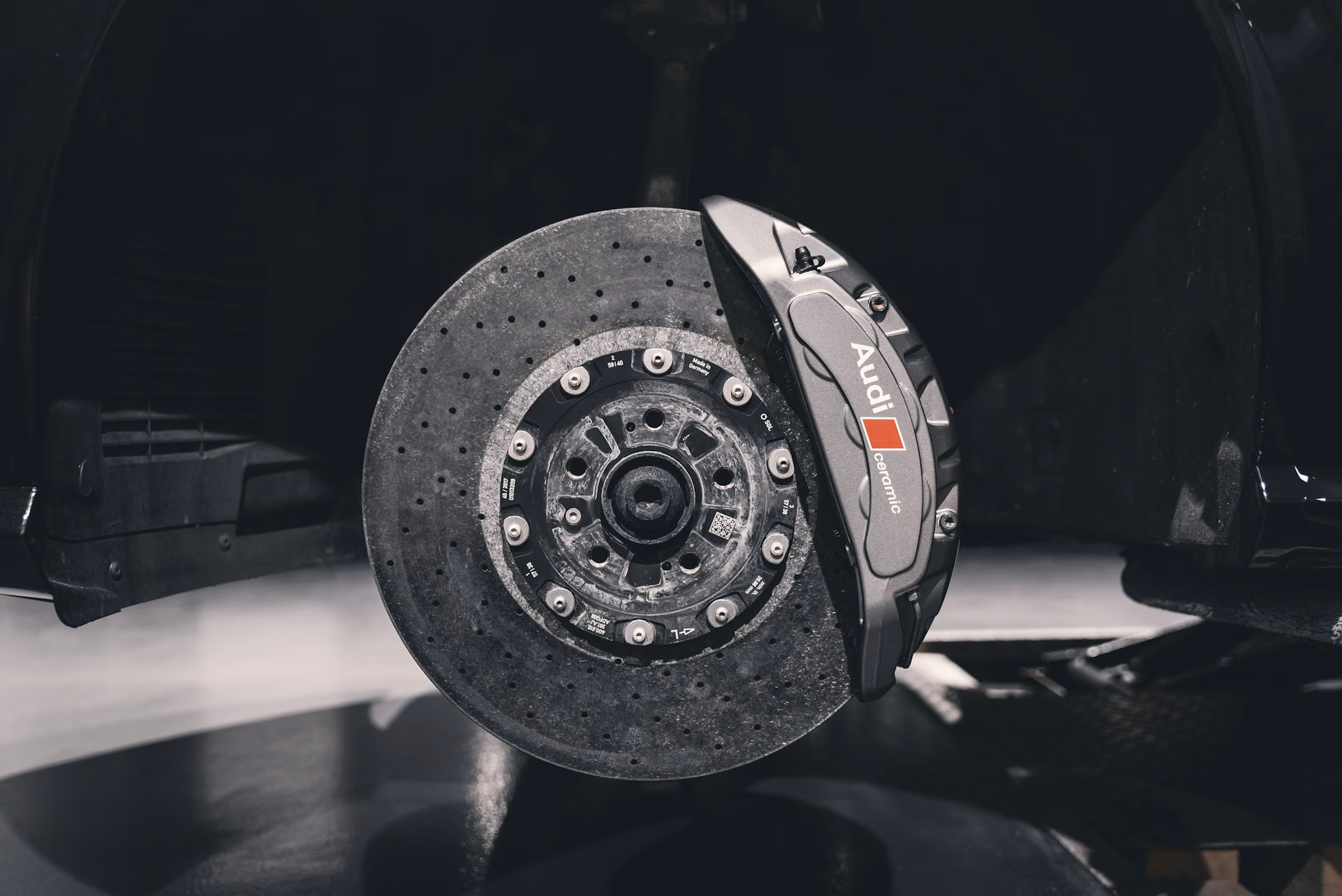 Close-up of an Audi ceramic brake rotor and caliper on a black car without the wheel.