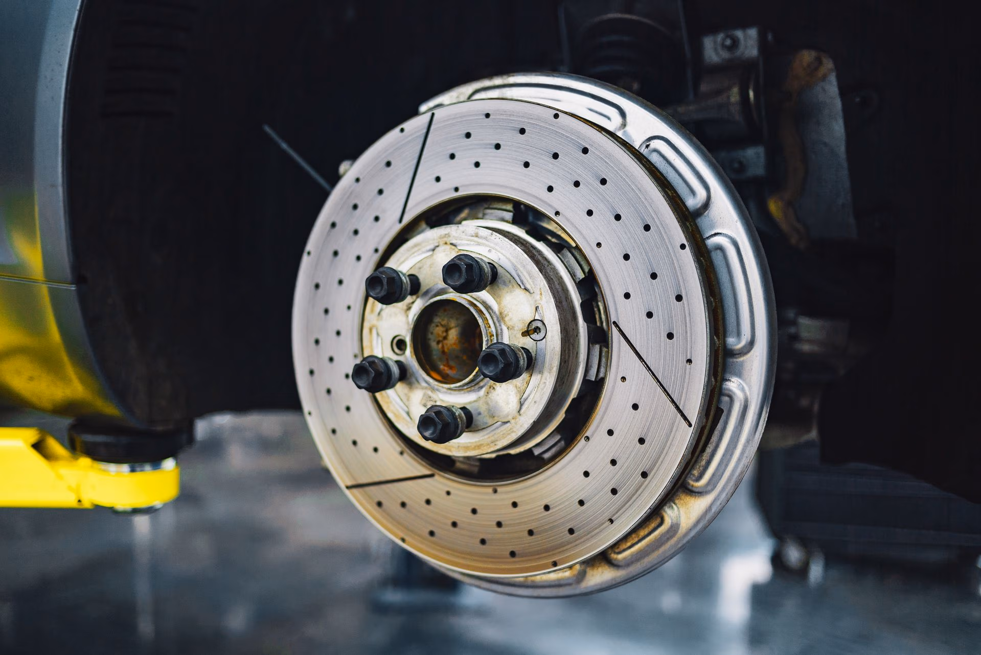 Close-up of a drilled and slotted car brake rotor mounted on wheel hub without the tire.
