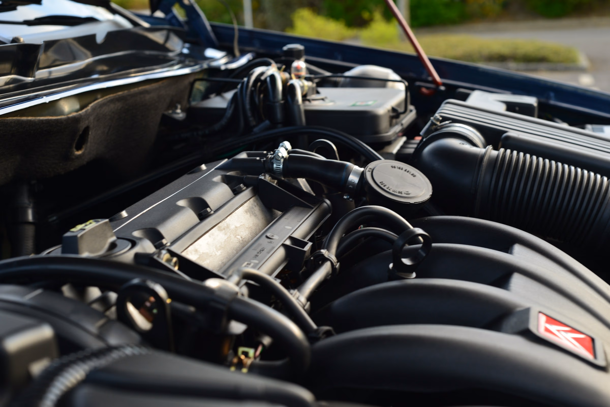 Close-up of a clean car engine with black plastic parts and hoses under an open hood.