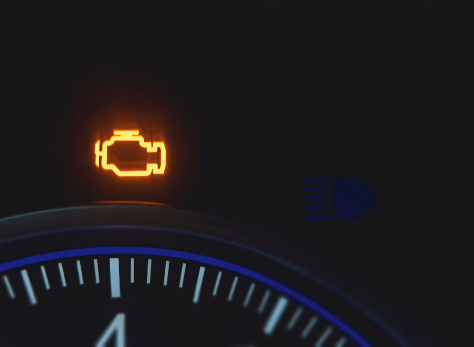 Orange illuminated check engine warning light on a car dashboard.