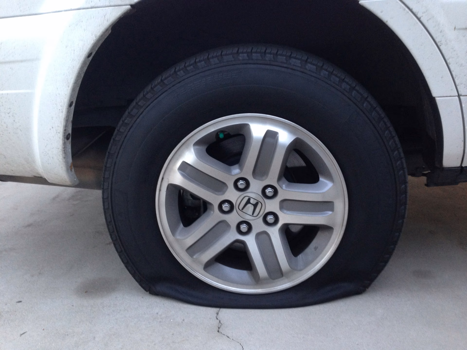 Flat tire on a white Honda vehicle with silver alloy wheel on a concrete surface.