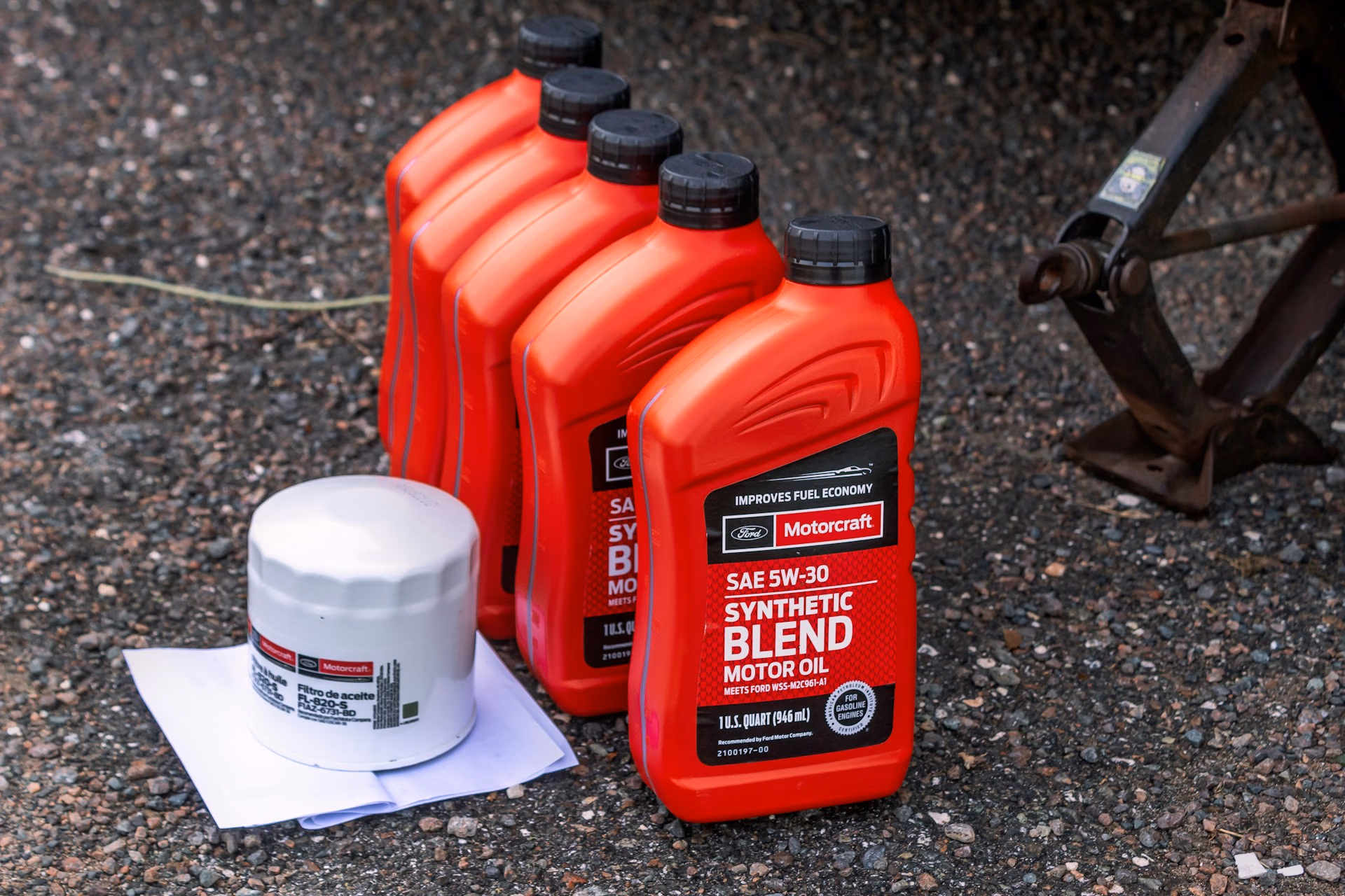 Five red Motorcraft synthetic blend motor oil containers and a white oil filter on gravel.