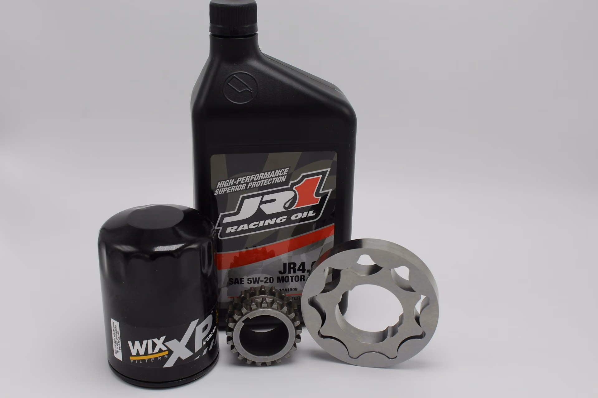 Black WIX XP oil filter, JR1 Racing Oil bottle, and two metal gear parts on a gray background.