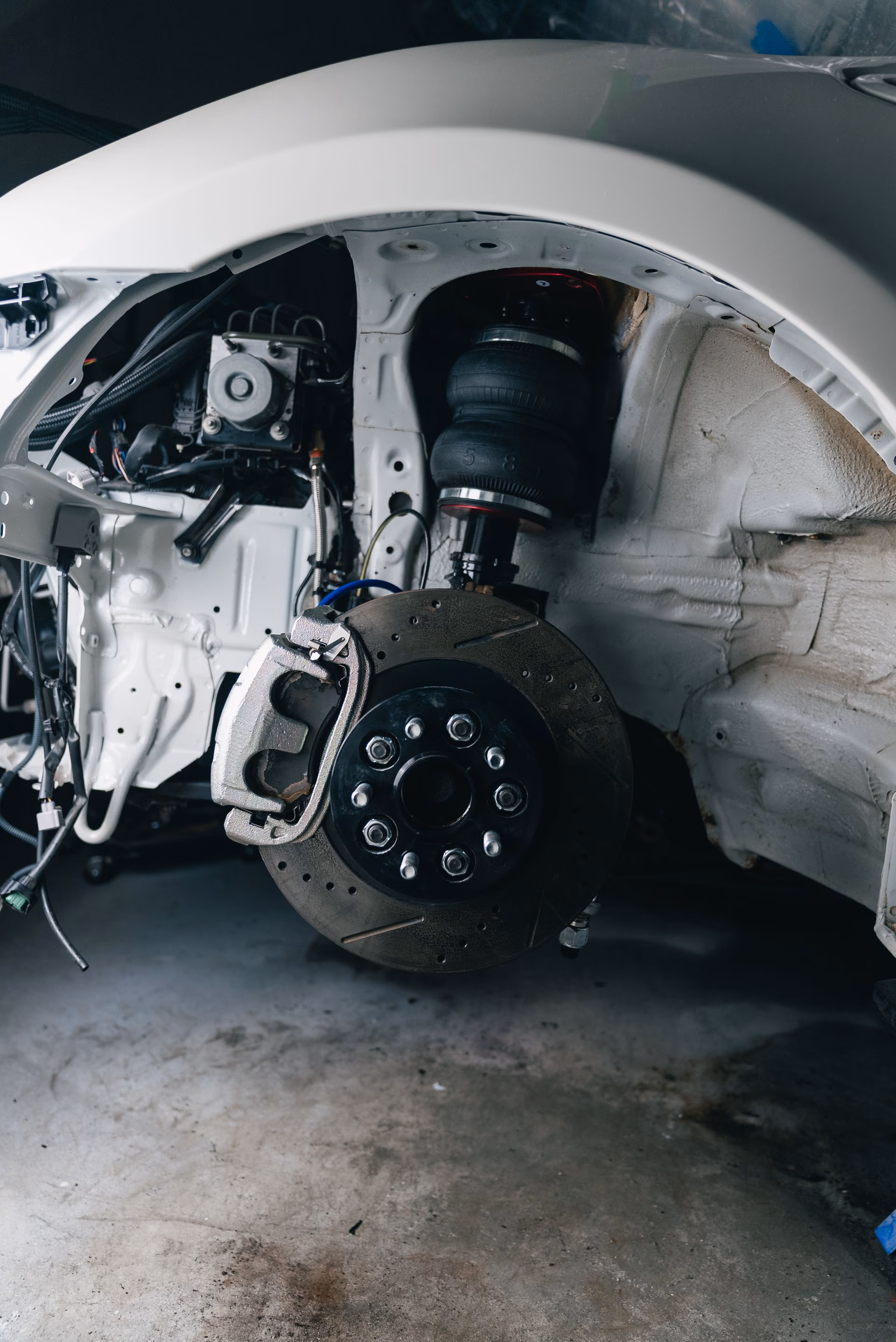 Close-up of a car's suspension and brake system with wheel removed in a garage.
