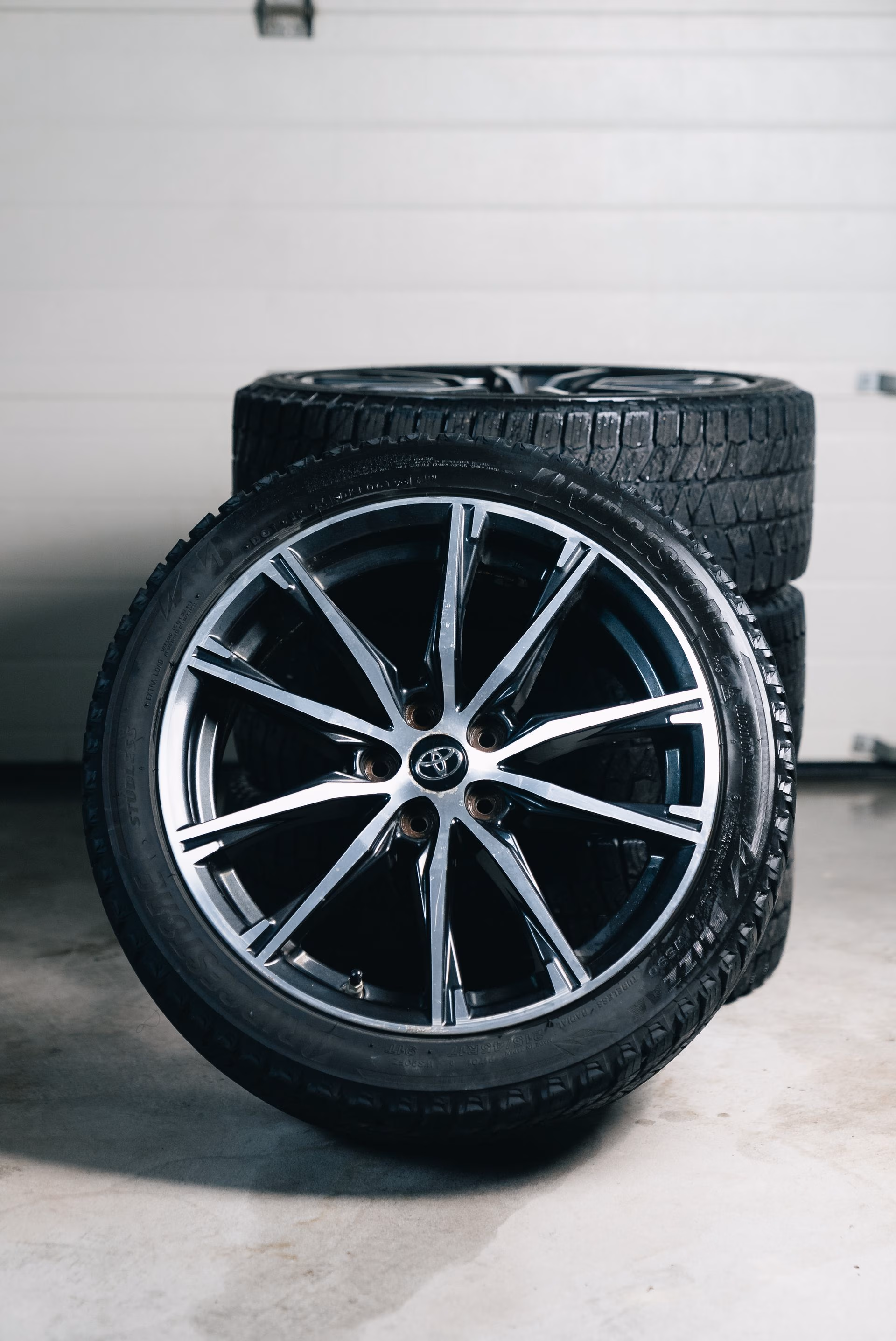Stack of four black car tires with alloy rims, one leaning in front showing Toyota logo in center.