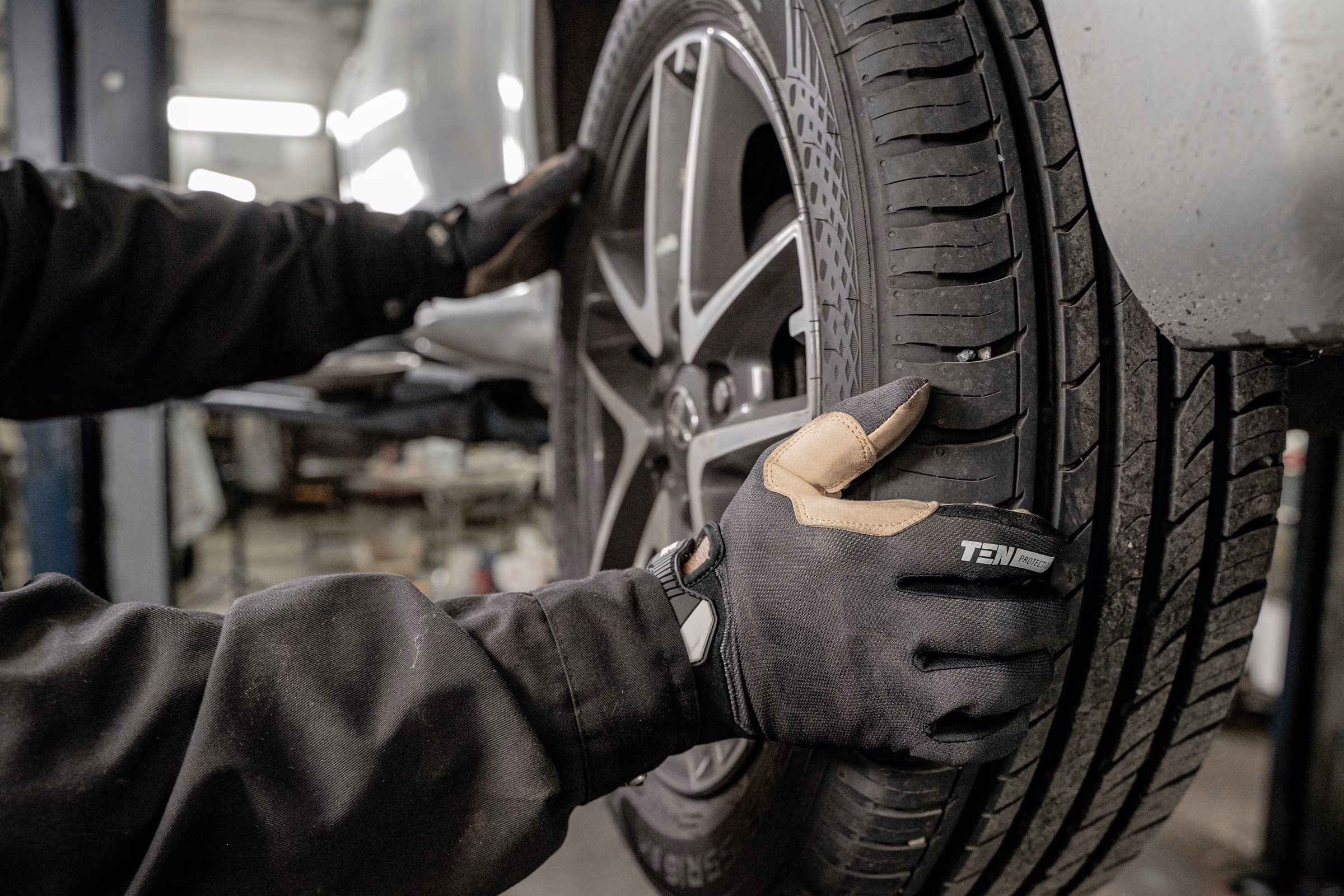 Gloved hands inspecting or adjusting a car tire’s tread at an auto repair shop.
